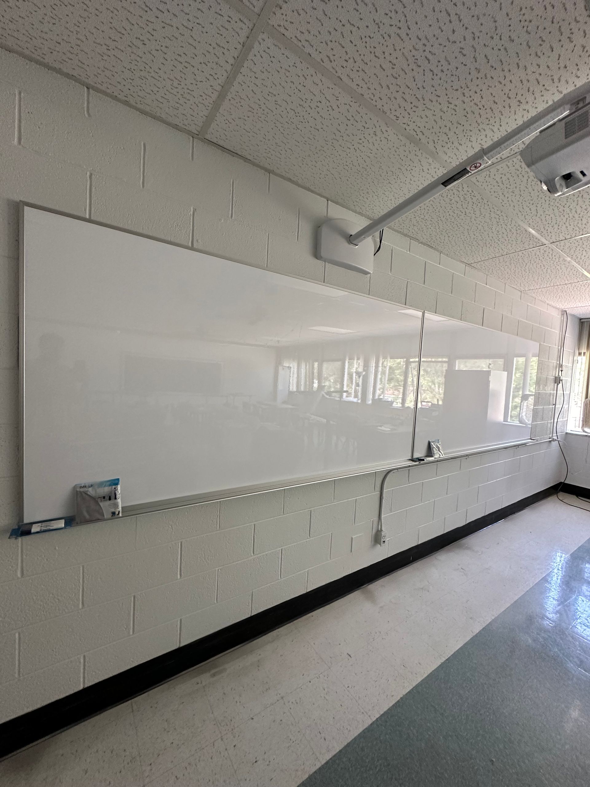 Empty classroom whiteboard on a tiled wall beneath a drop ceiling