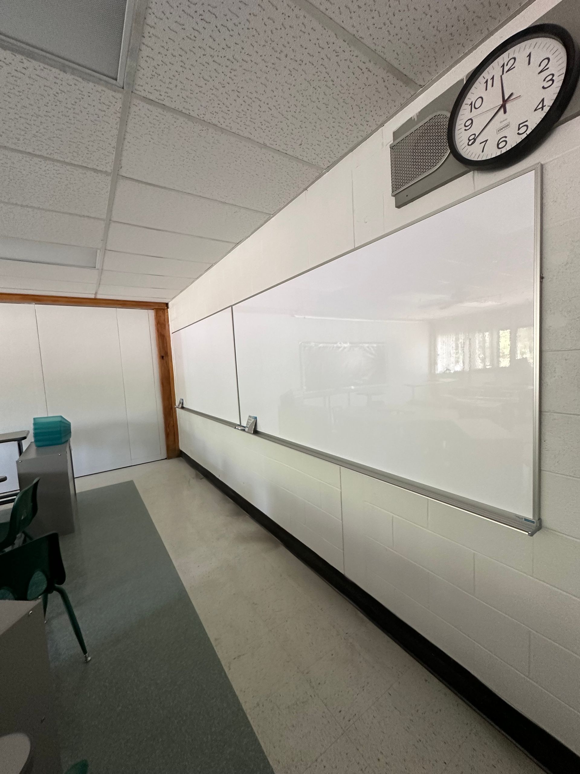 Empty classroom with a whiteboard, wall clock, and desks along the left side.