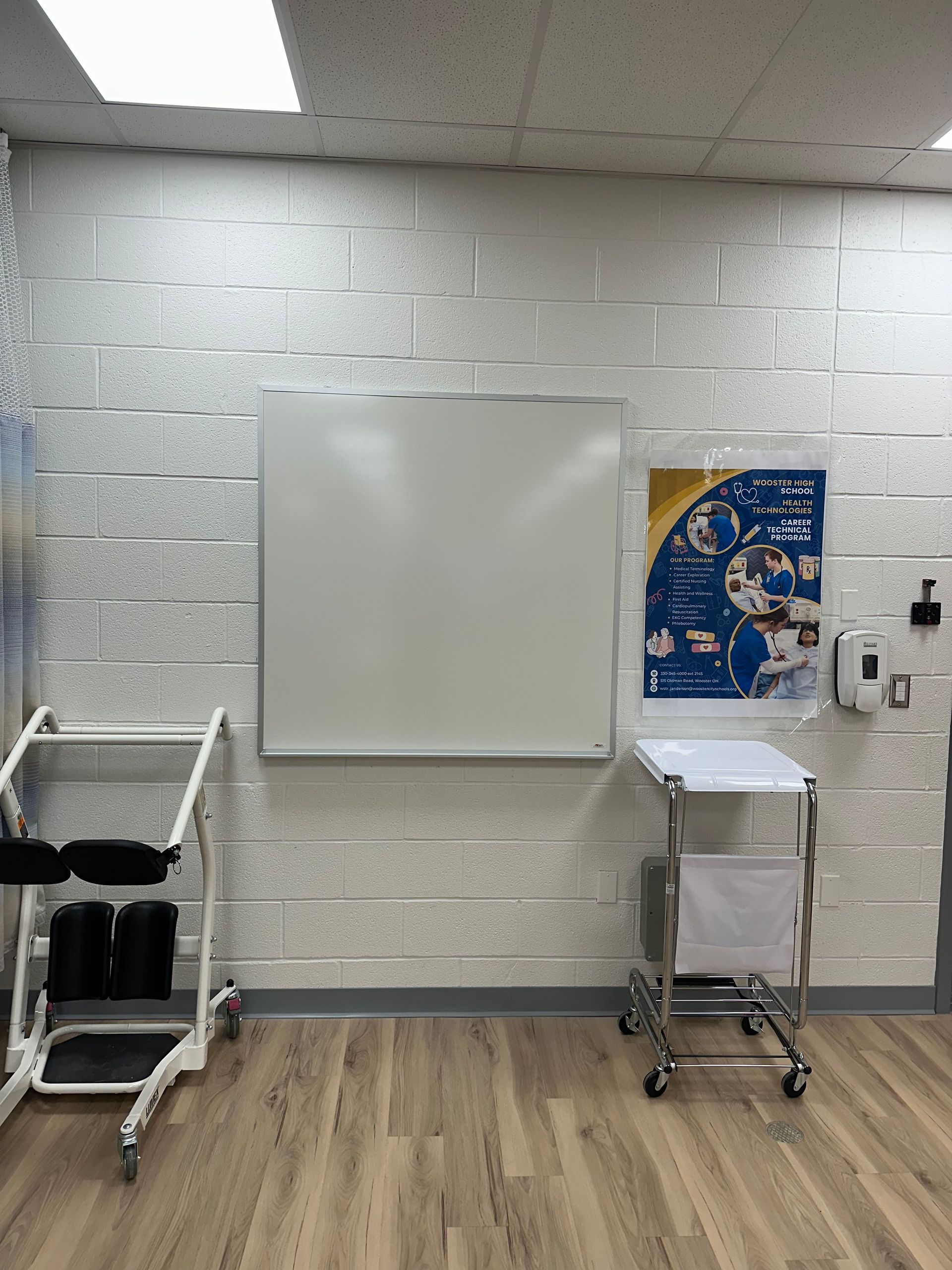 Small classroom with a whiteboard, rolling carts, and a blue educational poster on a cinderblock wall.