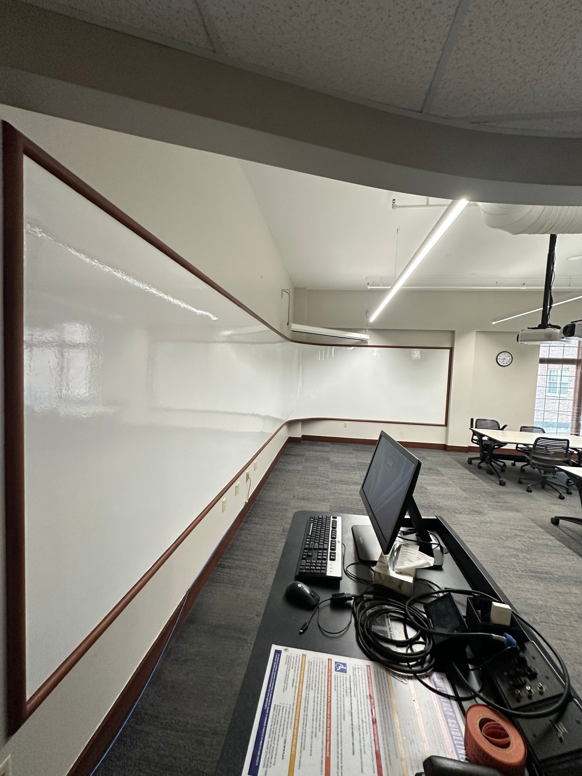 Empty classroom with whiteboard, desks, and monitors under fluorescent ceiling lights