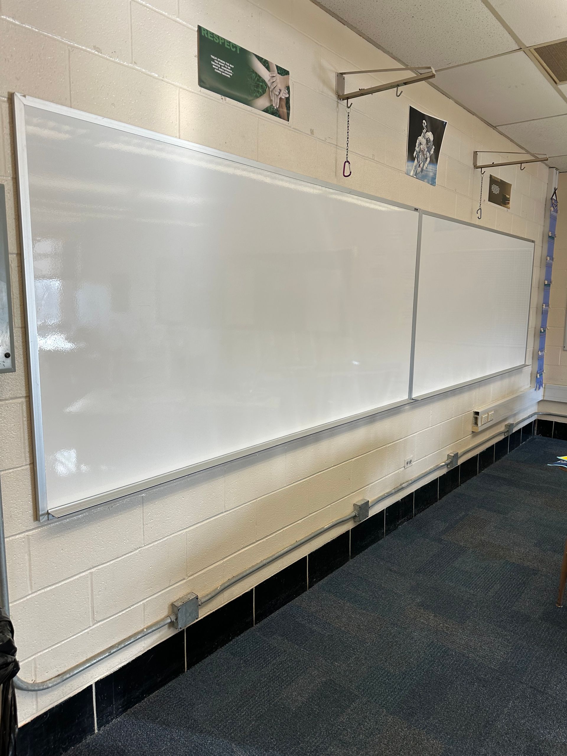 Empty classroom whiteboard mounted on a beige wall with posters above it