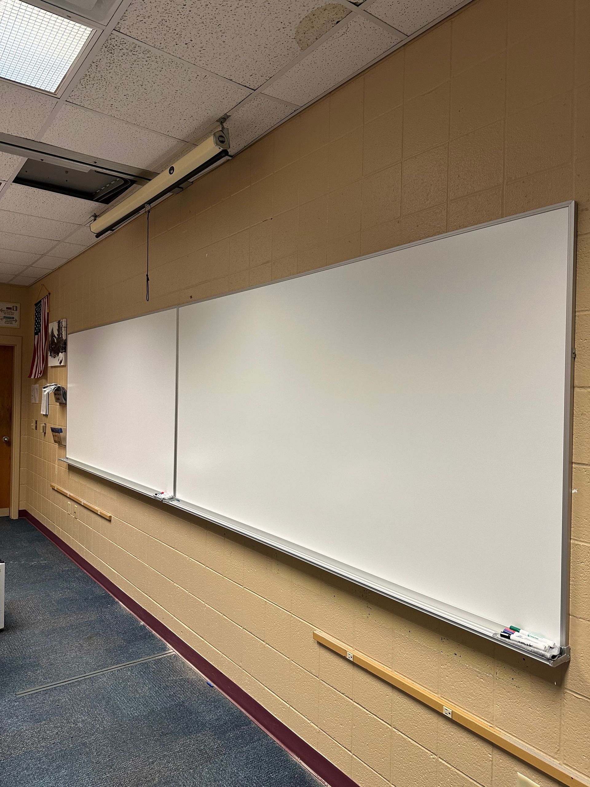 Empty classroom whiteboards on a beige wall with blue carpet and ceiling projector mount