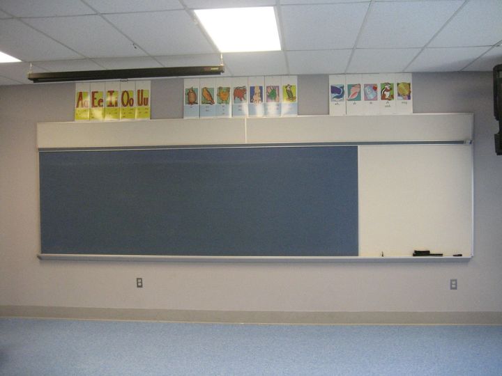 Empty classroom with a large blue chalkboard, whiteboard, and posters above the front wall.