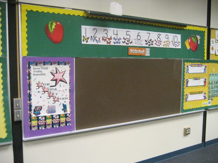 Classroom bulletin board with alphabet, numbers, red apples, and a large empty green display board