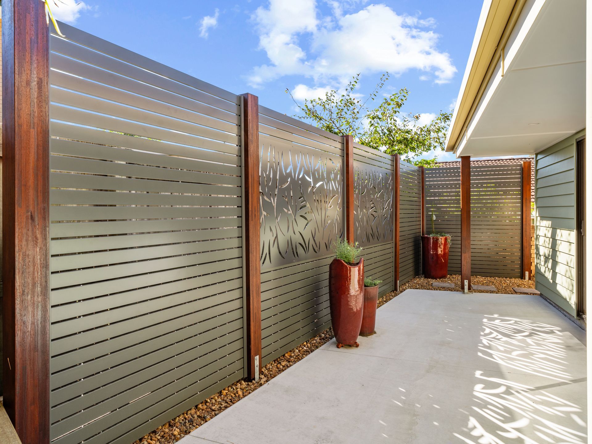 Modern patio with slatted privacy fence, large red planters, and bright blue sky.