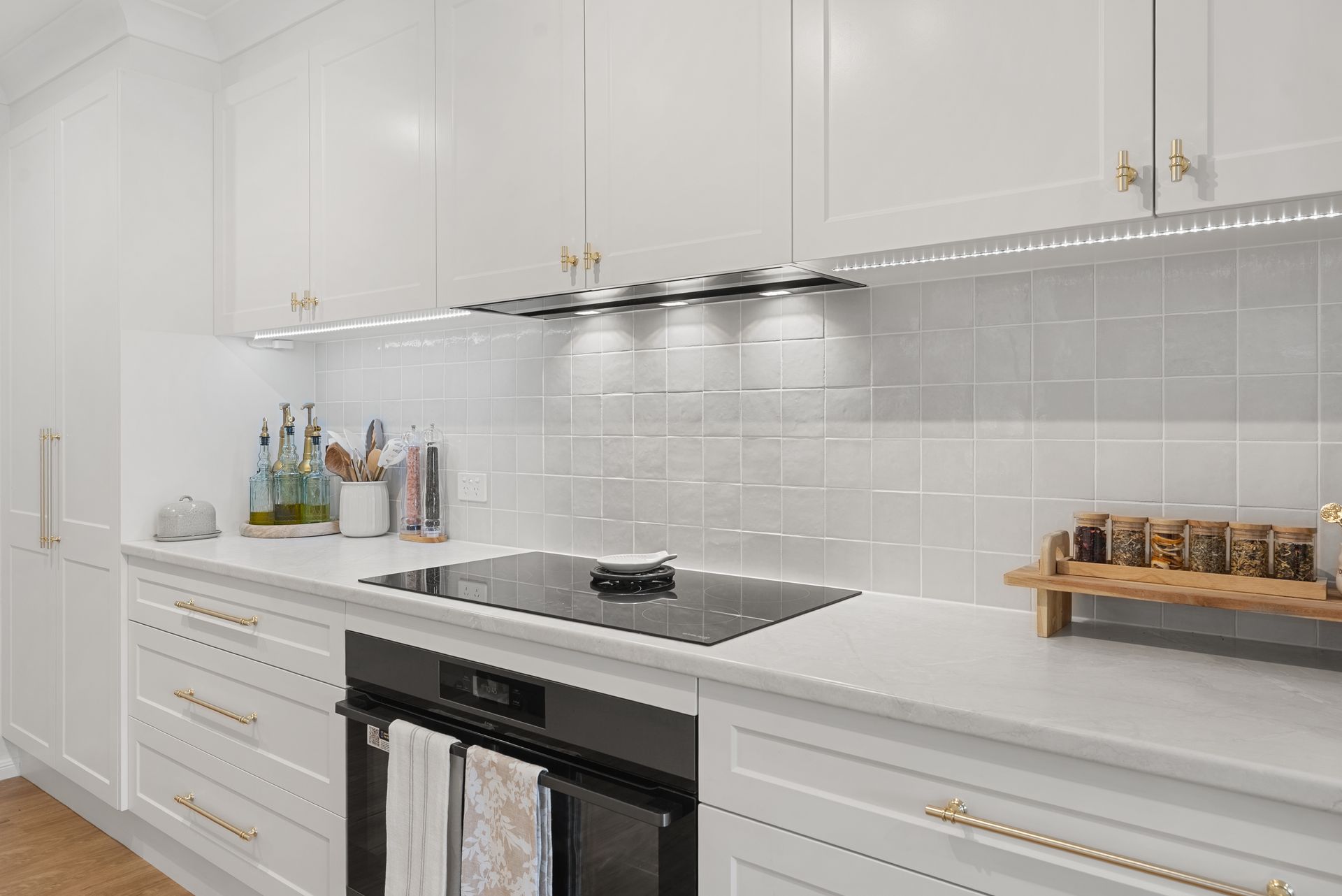 Bright white modern kitchen with built-in oven, stovetop, glossy cabinets, and tiled backsplash.