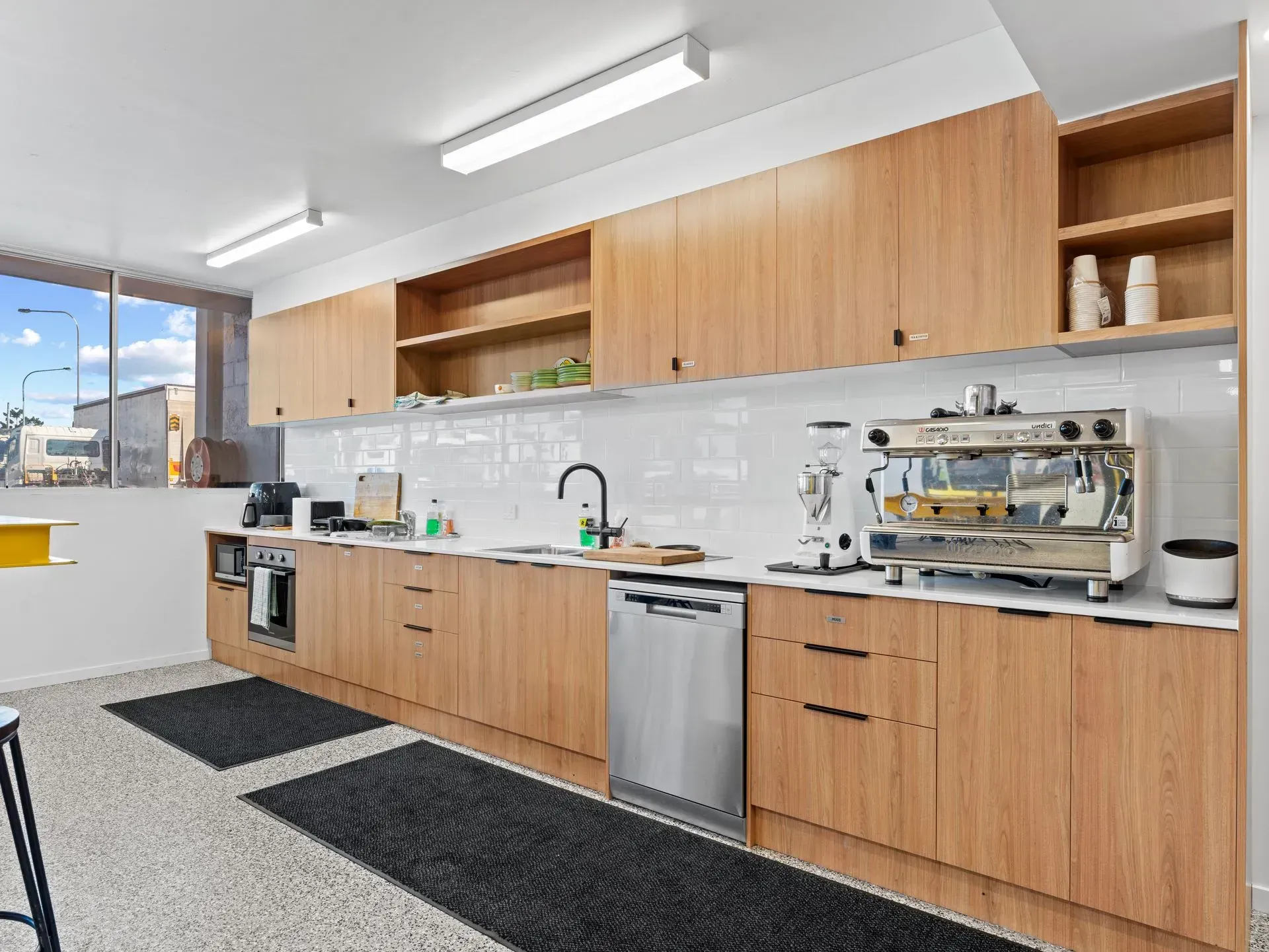 Bright modern kitchen with wooden cabinets, gray countertops, and stainless steel appliances under fluorescent lights