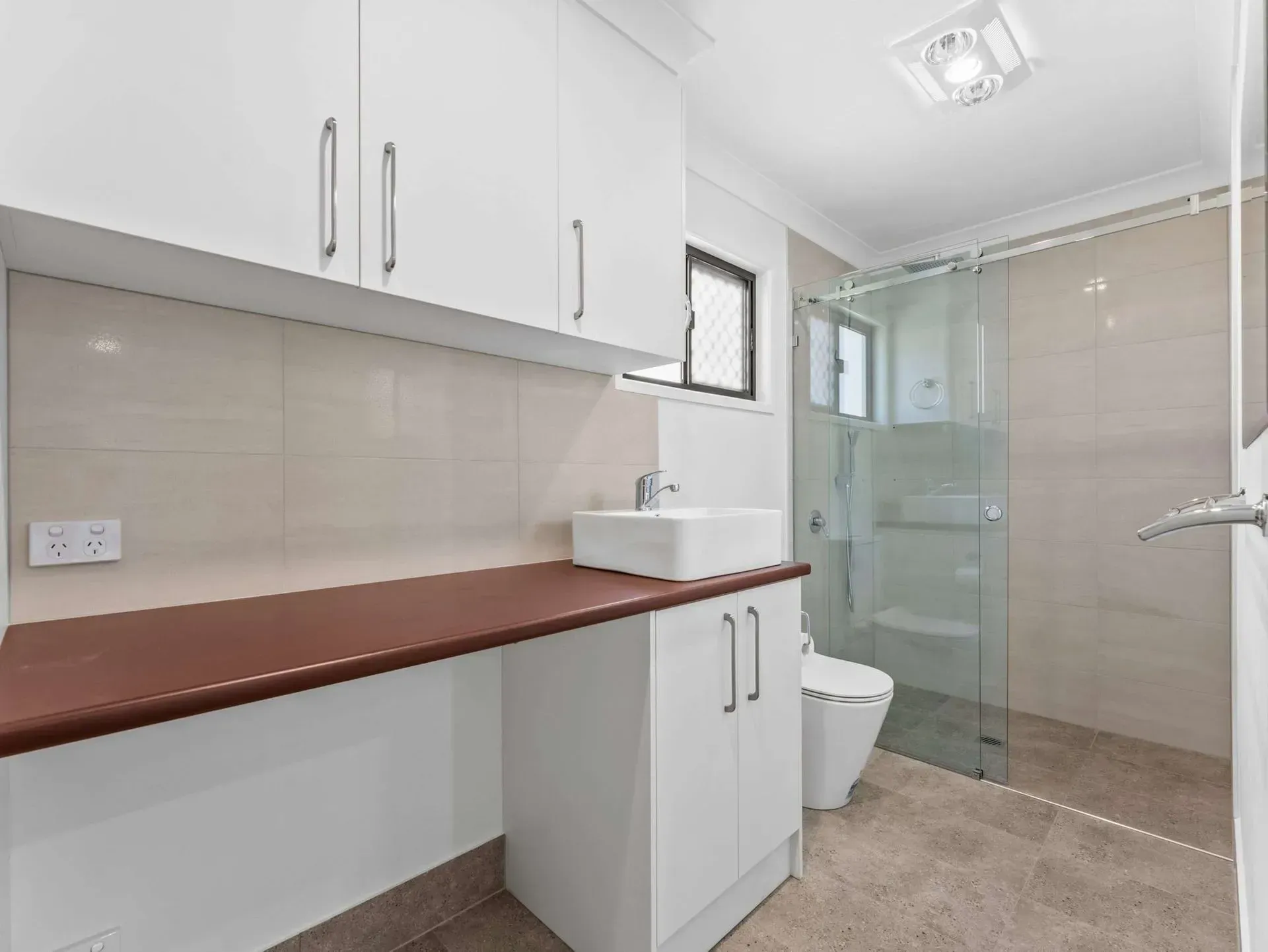 Modern bathroom with white cabinets, countertop sink, shower enclosure, and toilet in a bright, tiled space