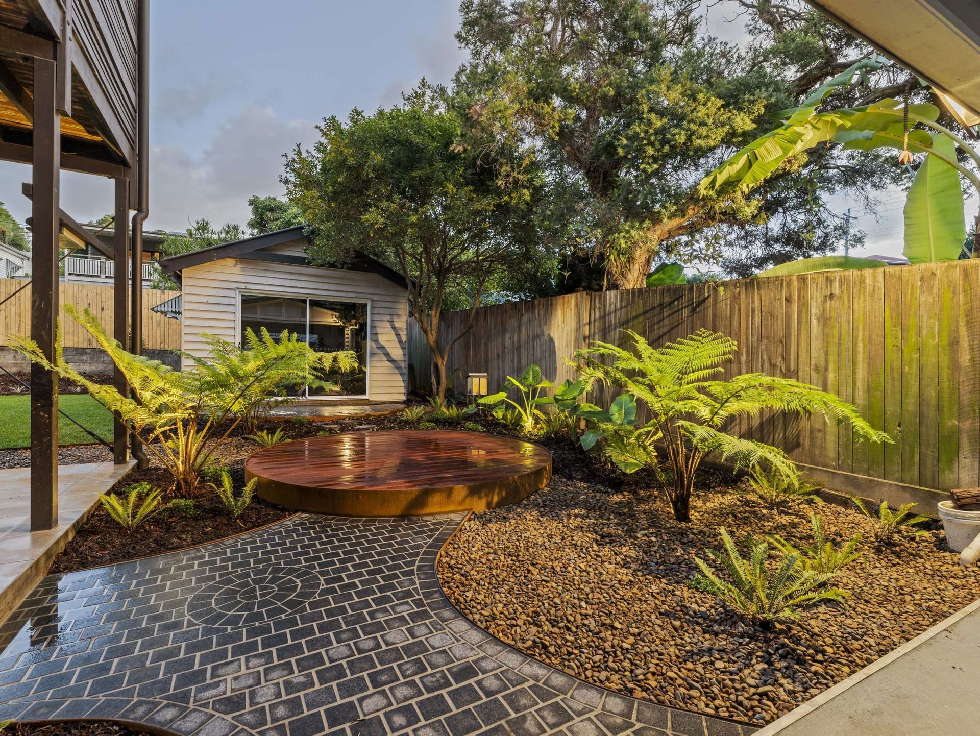 Garden path leading to a backyard with a rusted metal feature, ferns, and small shed.