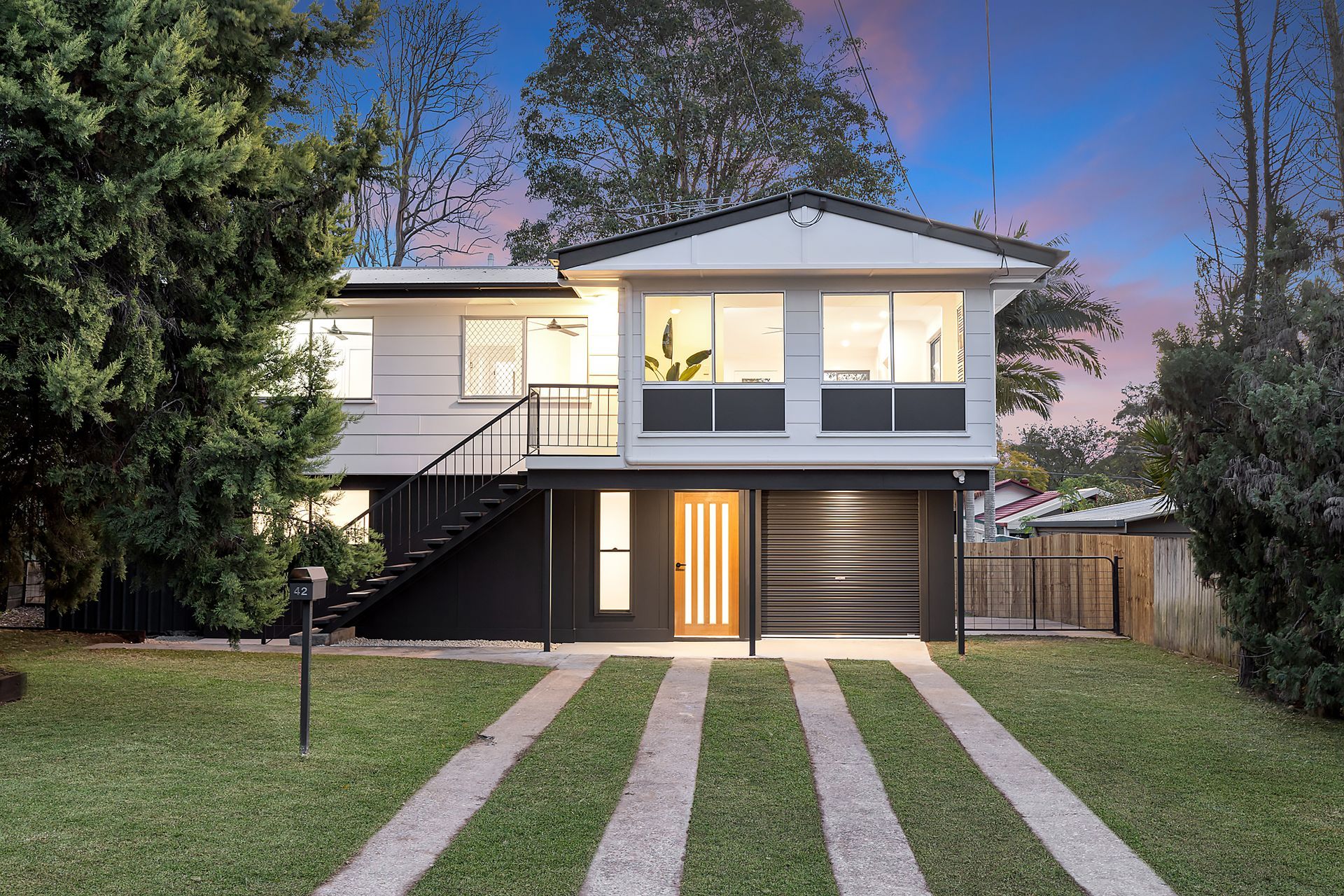 Two-story white house with black accents, driveway through grass, garage, and front door.