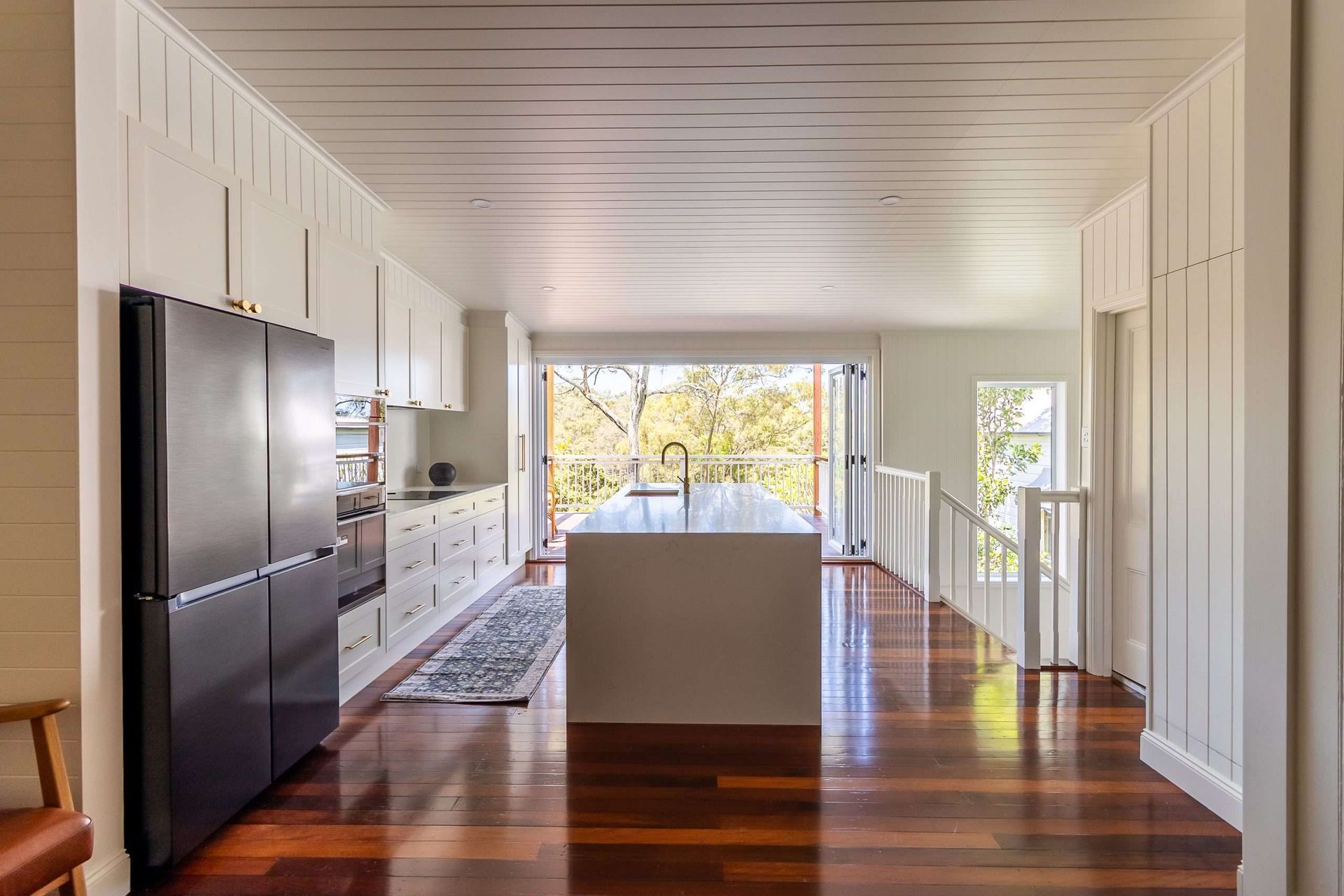 Bright modern kitchen with white cabinetry, dark wood floors, and a central island facing a sunlit window.