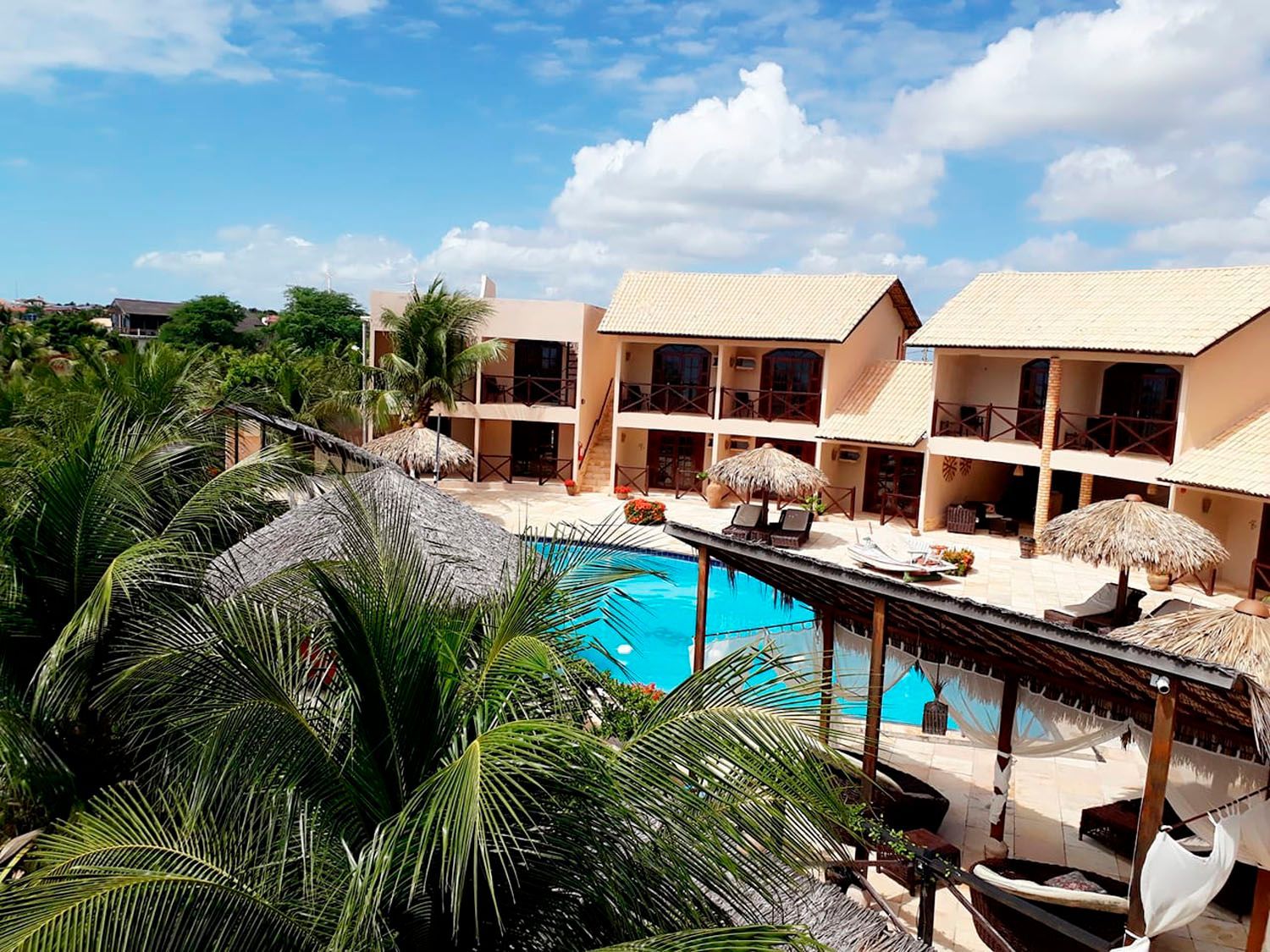 Uma vista aérea de um hotel com uma grande piscina cercada por palmeiras.