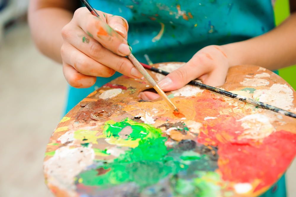 A Person Is Painting On A Palette With A Brush — The Red Chair Therapy in Blackwall, NSW