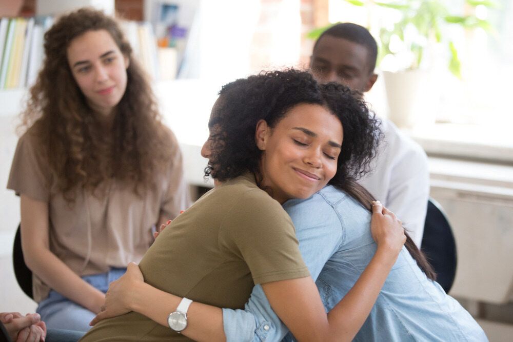 A Group Of People Are Hugging Each Other In A Room — The Red Chair Therapy in Blackwall, NSW