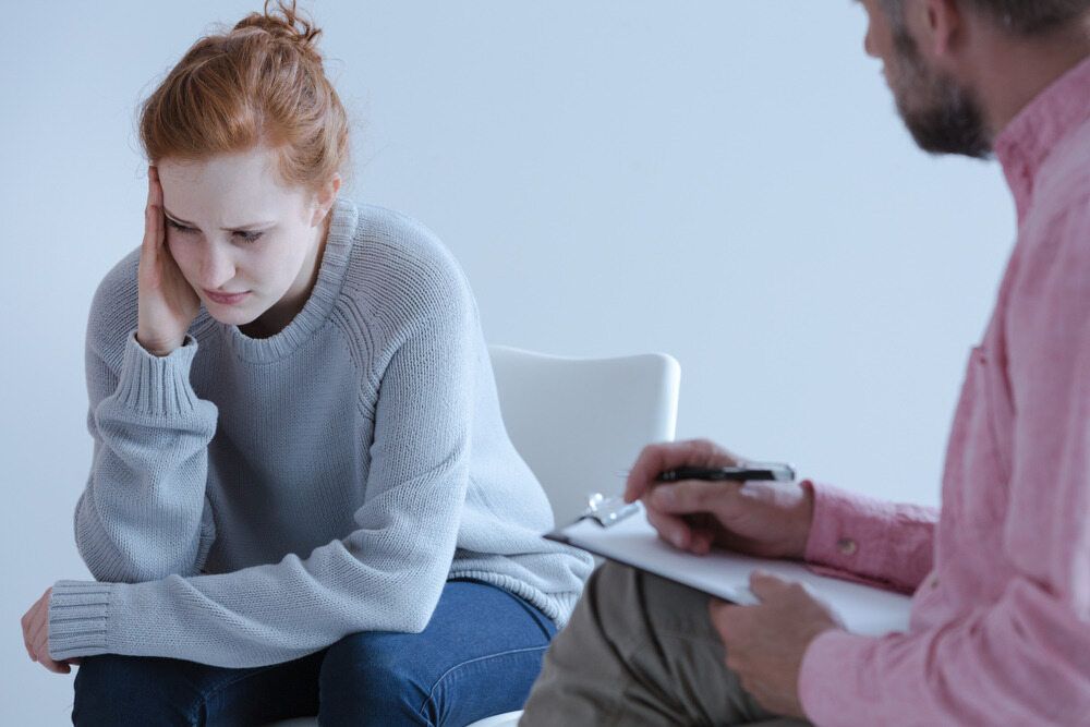A Woman Is Sitting In A Chair Talking To A Man In A Pink Shirt — The Red Chair Therapy in Blackwall, NSW