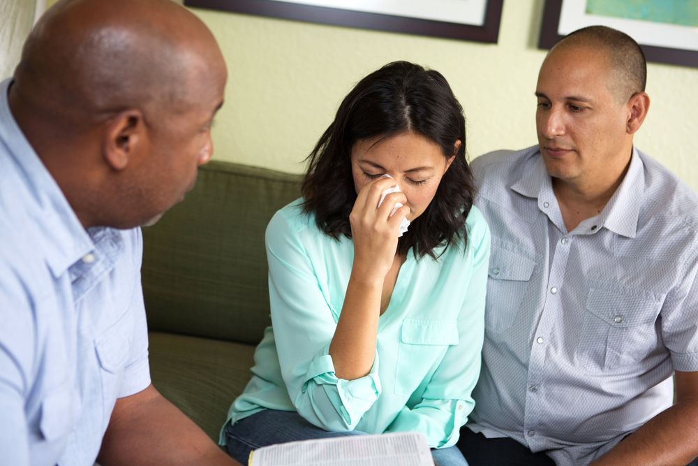 A woman is crying while sitting on a couch with two men.