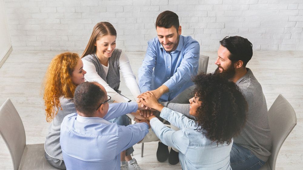 A Group Of People Are Sitting In A Circle Putting Their Hands Together — The Red Chair Therapy in Blackwall, NSW