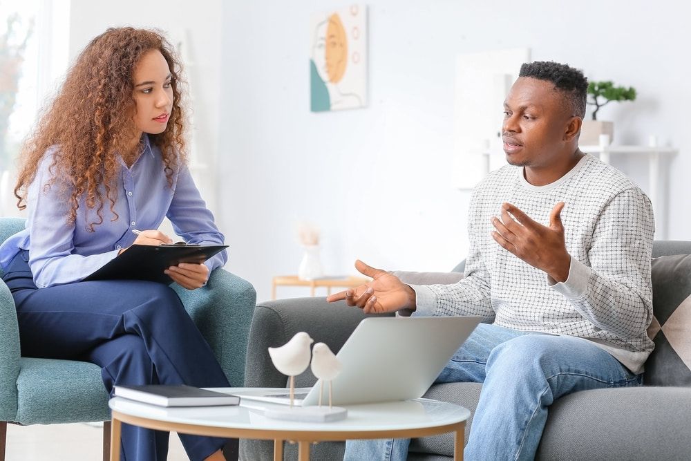 A Man And A Woman Are Sitting On A Couch Talking To Each Other — The Red Chair Therapy in Blackwall, NSW