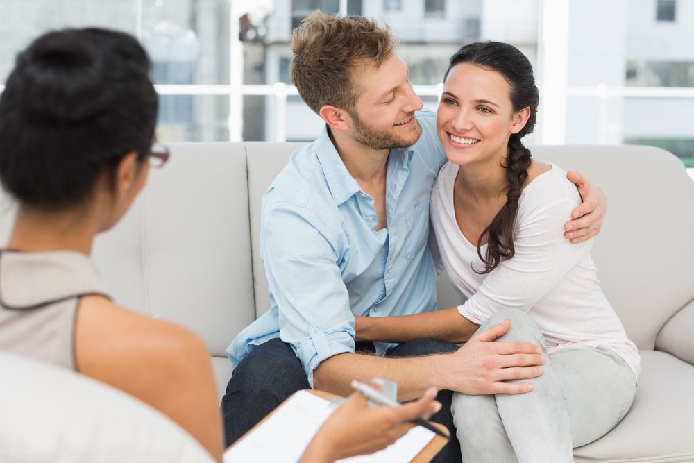 A Man And A Woman Are Sitting On A Couch Talking To A Woman — The Red Chair Therapy in Blackwall, NSW