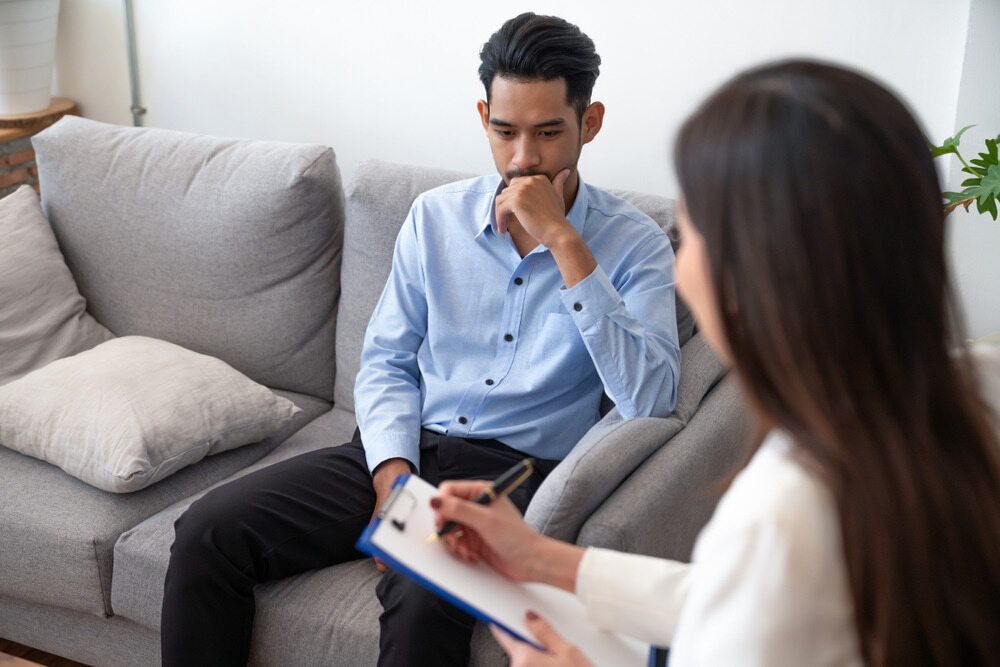 A Man Is Sitting On A Couch Talking To A Woman — The Red Chair Therapy in Blackwall, NSW