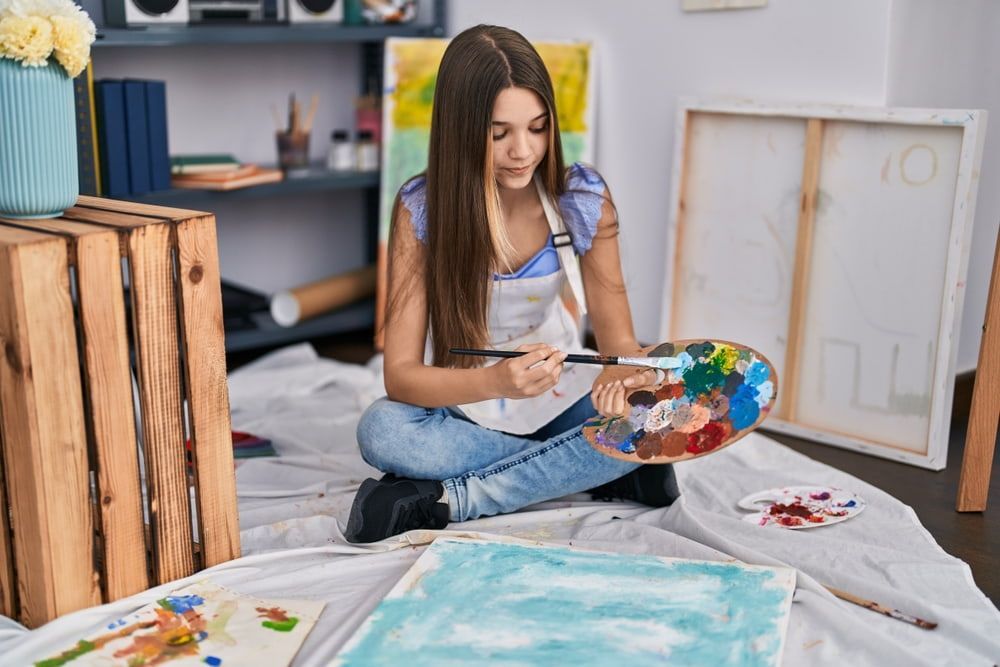 A Young Girl Is Sitting On The Floor Painting A Picture — The Red Chair Therapy in Blackwall, NSW