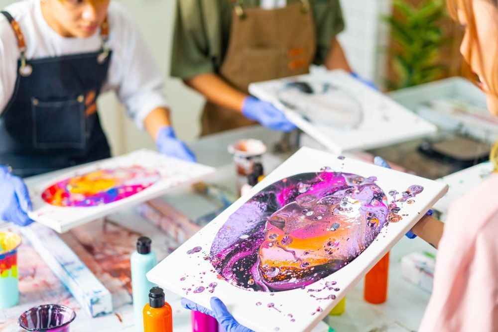 A Group Of People Are Sitting At A Table Holding Paintings — The Red Chair Therapy in Blackwall, NSW