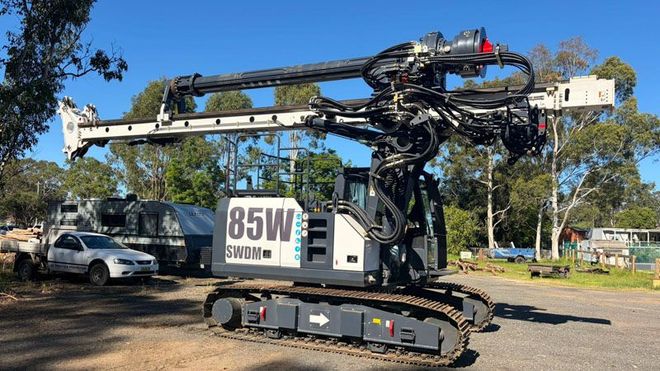 Tracked drilling rig with extended boom and hoses parked on a roadside in daylight