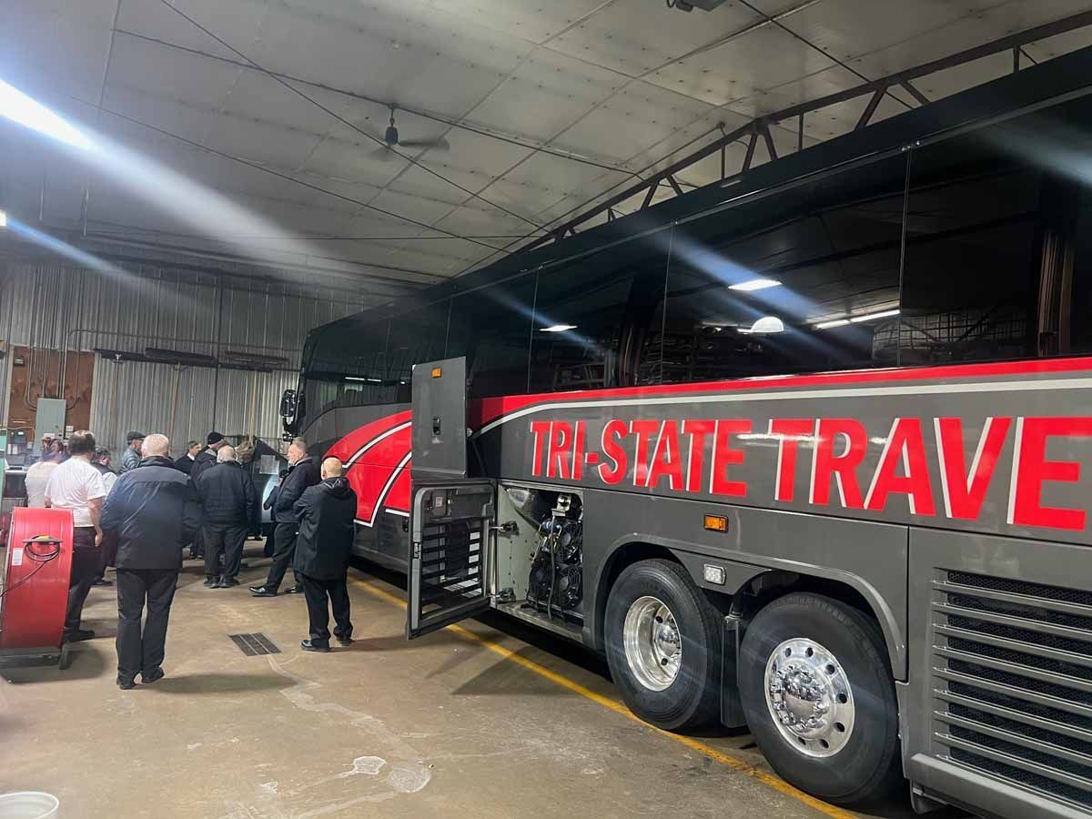 Crowd beside a black and red bus under a large tent, with โSTATE TRAVELโ on the side.
