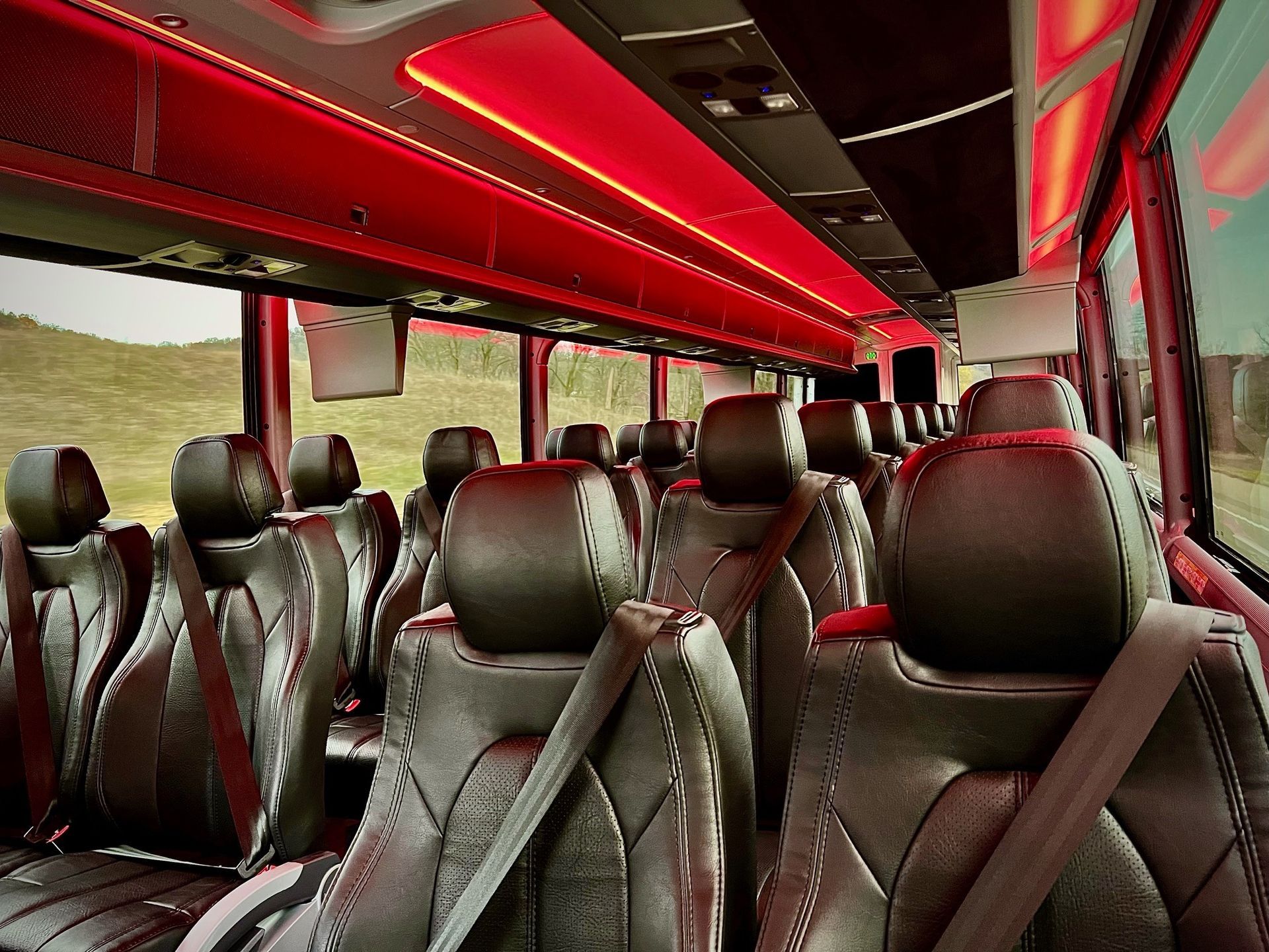 Empty bus interior with red ceiling lighting and rows of black leather seats