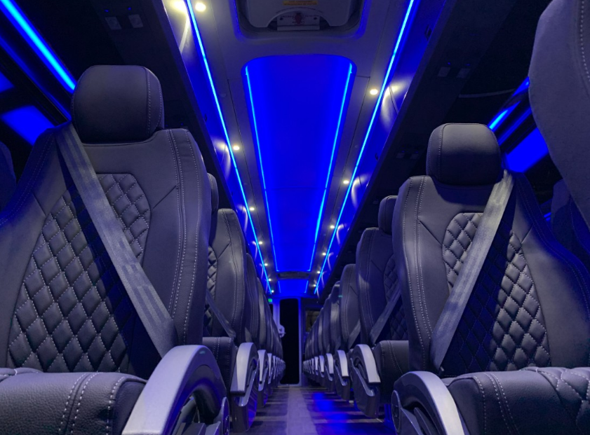 Luxury bus interior with blue LED lighting and quilted gray seats, viewed down the aisle