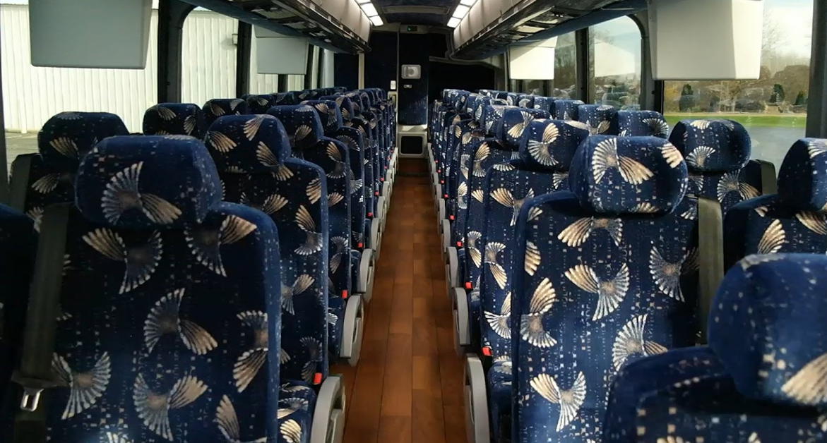 Empty bus interior with blue patterned seats and a wooden aisle.
