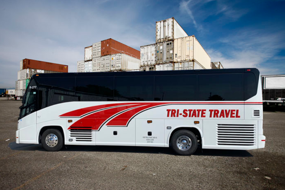 White Tri-State Travel coach bus with red stripes parked in an industrial lot