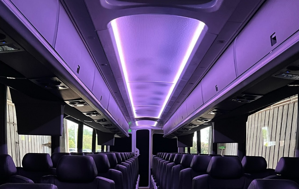 Empty luxury bus interior with purple LED ceiling lights and rows of black seats