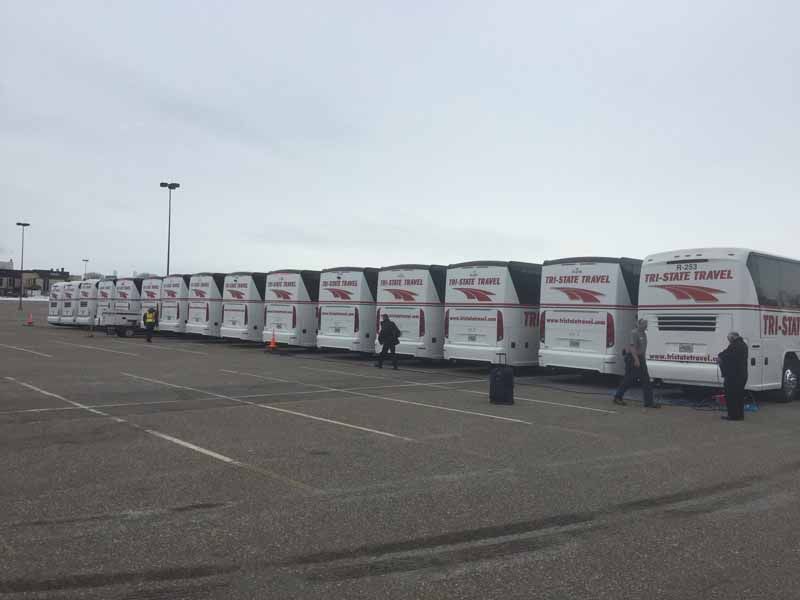 Row of white tour buses parked in a lot under an overcast sky