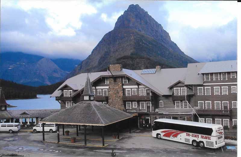 Mountain village with wooden buildings, a bus, and a dramatic peak under cloudy skies