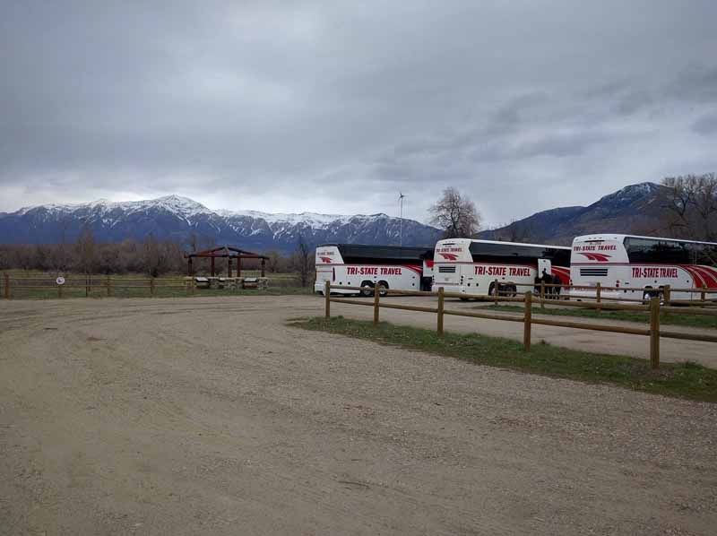 Snowy mountains behind a fenced field with parked white buses under a cloudy sky