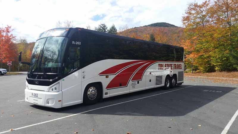 White and red coach bus parked in a lot with autumn trees in the background