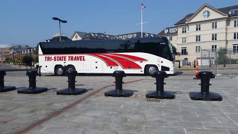 White and red TPL shuttle bus parked by a waterfront plaza with black bollards and buildings in the background