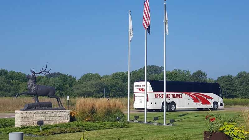 UPS delivery truck beside flags and a deer statue in a grassy roadside area