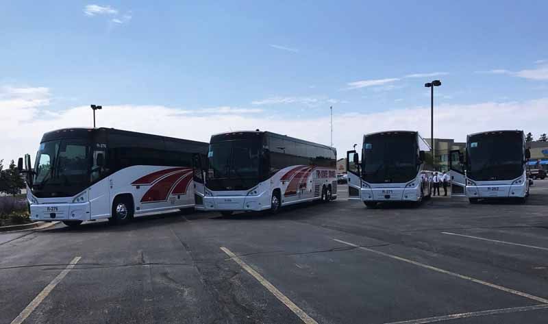 Four white coach buses parked in a lot under a bright sky.