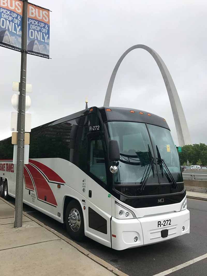 White and black coach bus parked by a street, with the Gateway Arch in the background.