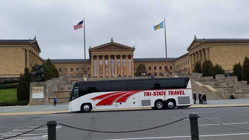 White tour bus passes the Philadelphia Museum of Art steps under U.S. and Ukrainian flags