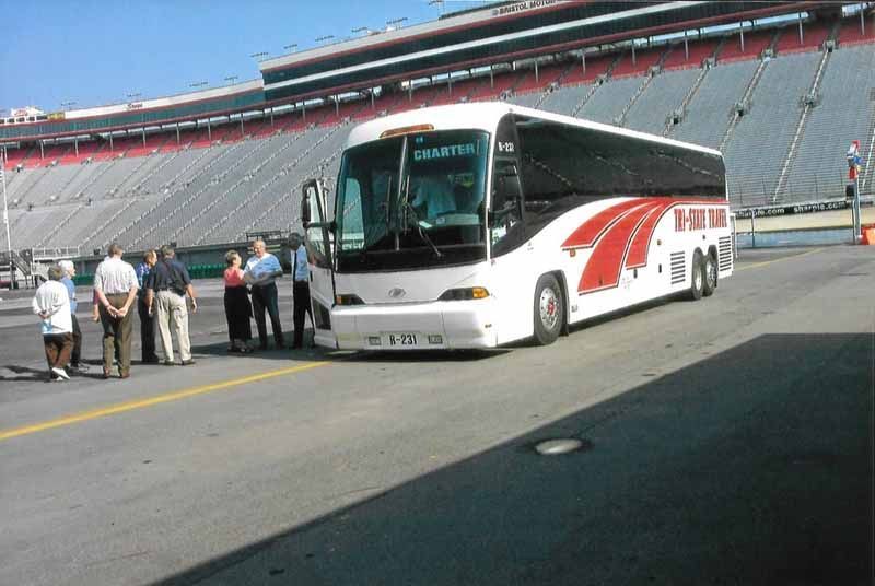 White tour bus on a racetrack with a small group of people standing nearby
