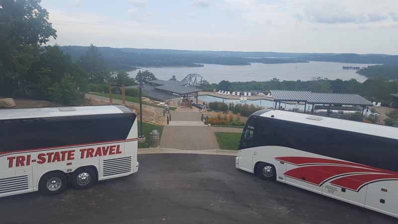 Two parked tour buses overlooking a lake and waterfront from a hillside lot