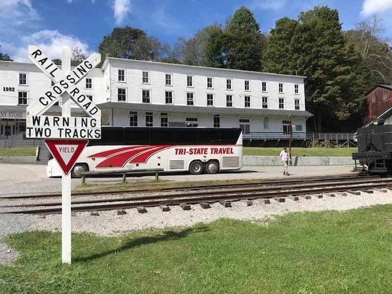 White museum building behind railroad tracks with a train car and a railroad crossing sign in the foreground