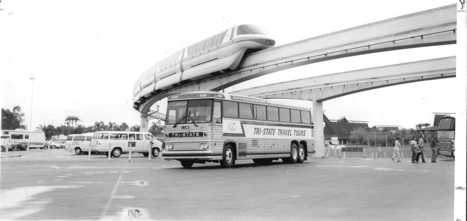 Black-and-white photo of a bus driving under a futuristic elevated monorail track.