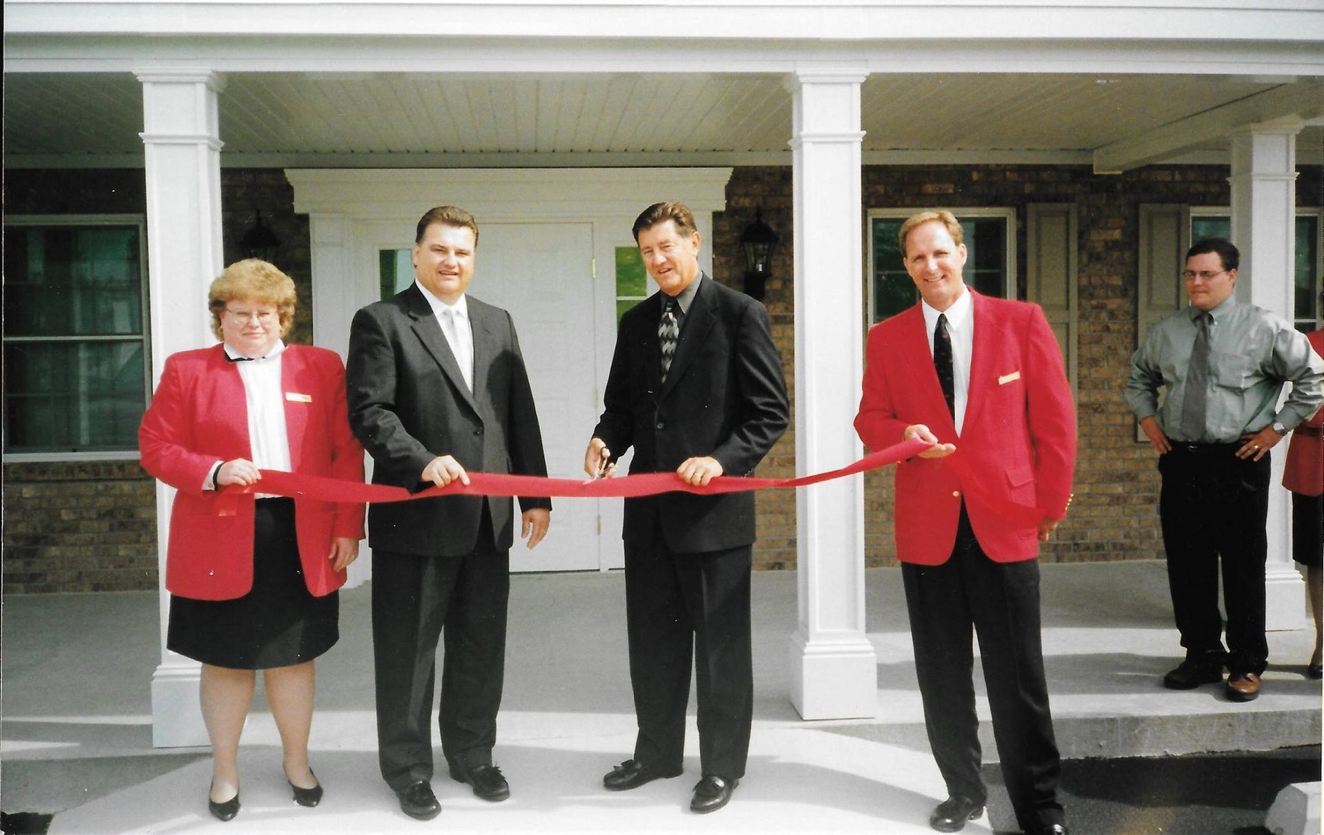 Ribbon-cutting ceremony with four people in red jackets holding scissors outside a building