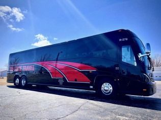 Sleek black and red charter bus parked on a sunny road under a blue sky