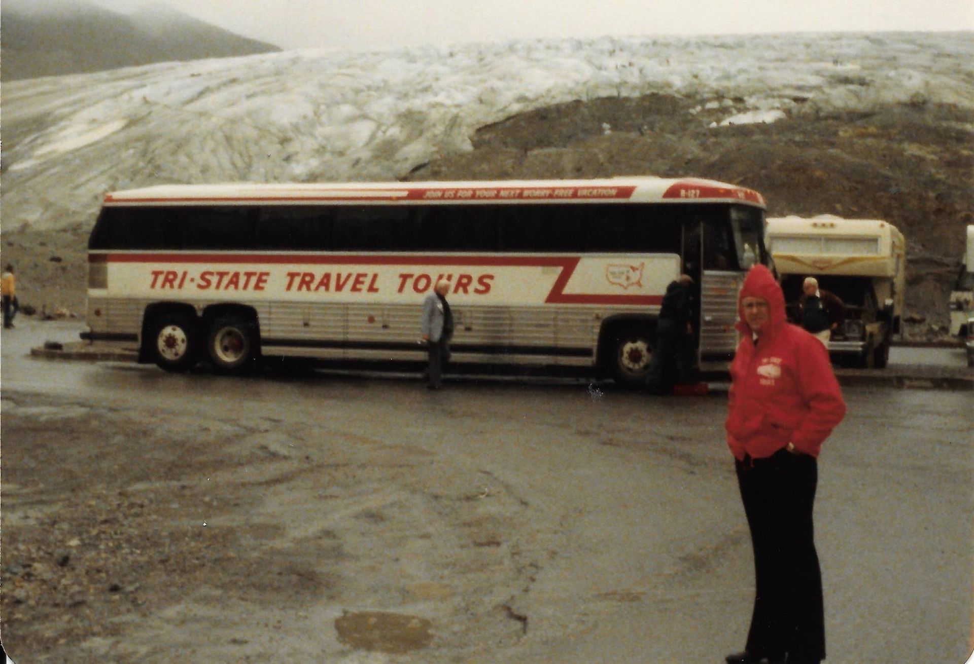 Tour bus parked by a glacier, with a person in a red jacket standing nearby.