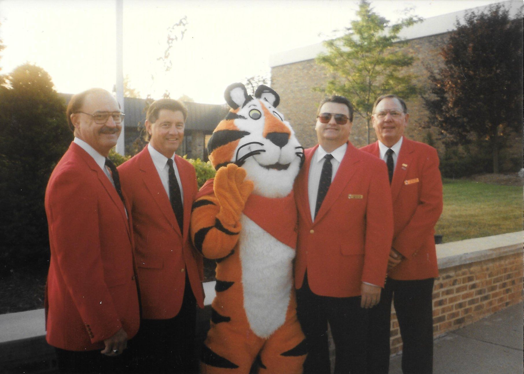Five men in red blazers stand with the Tiger mascot outdoors in front of a building.
